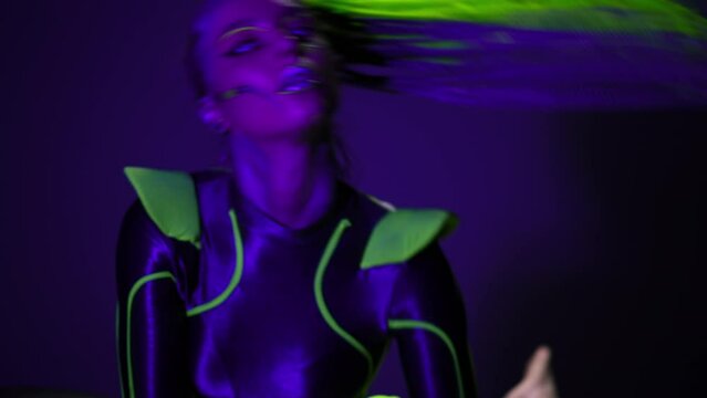Portrait of bright woman with fluorescent makeup in costume dancing in darkness in neon light. Extraordinary young slim flexible artist performing posing looking at camera