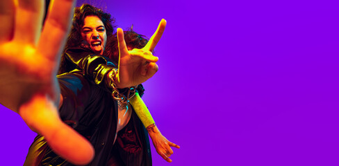 Close-up hands of young couple of rock-and-roll musicians wearing black leather outfits gesturing, shouting on blue yellow background in neon light. Flyer
