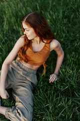 Happy redheaded woman sitting on fresh spring green grass in the garden smiling and looking out into the sun, view from above, harmony with nature