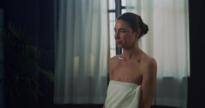 Cinematic shot of young woman in white bathrobe is applying female antiperspirant body spray deodorant on her armpit after shower during personal beauty hygiene routine at home before going out.