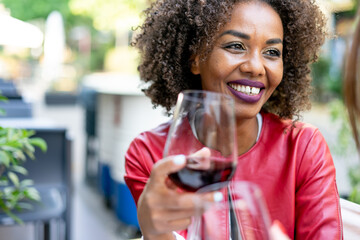 Happy african american woman drinking red wine at bar restaurant while having a dating- Multiracial friends celebrating at happy hour  - Friendship and happiness concept.
