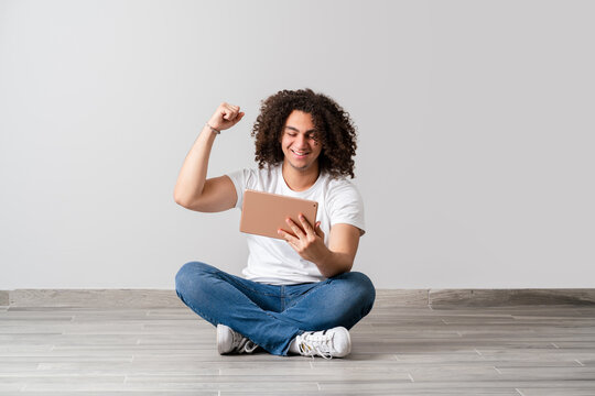 Young man with curly hair hold his fist up and become happy, while he see the results on the screen. Victory and success concept