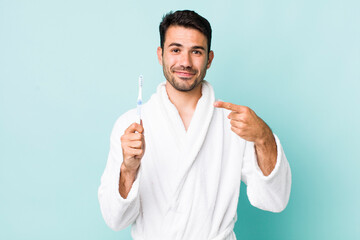 young adult hispanic man smiling cheerfully, feeling happy and pointing to the side. toothbrush concept - obrazy, fototapety, plakaty