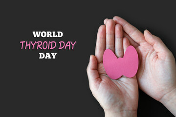 Obraz premium World Thyroid Day. Adult hands hold paper form of the thyroid gland on black background. Problems with thyroid. Polycystic disease.