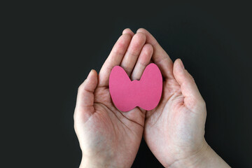 Obraz premium World Thyroid Day. Adult hands hold paper form of the thyroid gland on black background. Problems with thyroid. Polycystic disease.