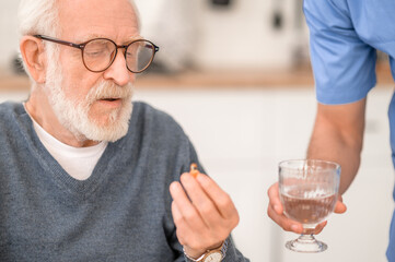 Pensioner taking a pill with water supervised by his caregiver
