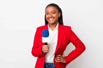 young adult black woman smiling happily with a hand on hip and confident. presenter and microphone concept - obrazy, fototapety, plakaty
