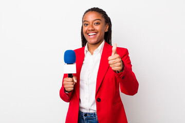 young adult black woman feeling proud,smiling positively with thumbs up. presenter and microphone...