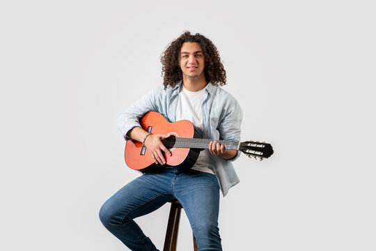 Young man with curly hair, playing acoustic solo guitar, isolated on white background