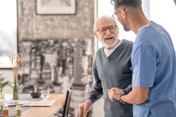 Old man standing by the table supported by a nurse