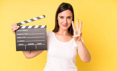 young adult pretty woman smiling and looking friendly, showing number three. cinema clapper concept