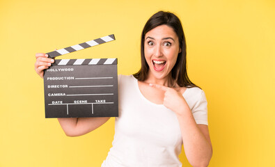 young adult pretty woman looking excited and surprised pointing to the side. cinema clapper concept
