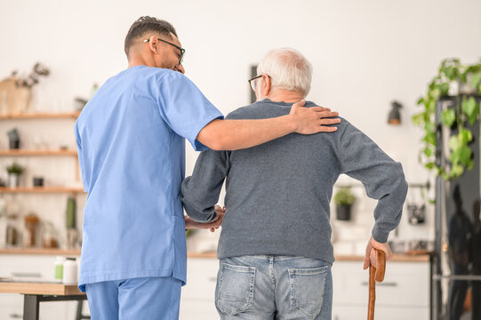 Medical worker assisting his patient to walk with a cane