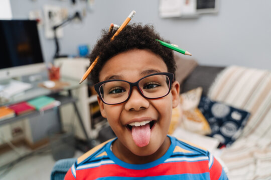 Black boy showing his tongue while making fun with pencils