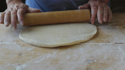 The process of making pizza or bread dough according to traditional recipes at home. Old woman hands roll out the dough on a wooden board
