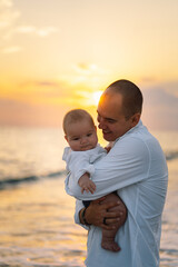 Happy Father's day. Father and baby play on the beach. Dad and him Child together enjoying sunset. Loving single father hugs cute little son.