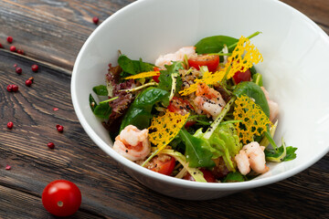 Salad with shrimps and tomatoes. On a wooden table.