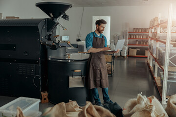 Business owner of coffee factory working laptop on background of coffee roasting machine