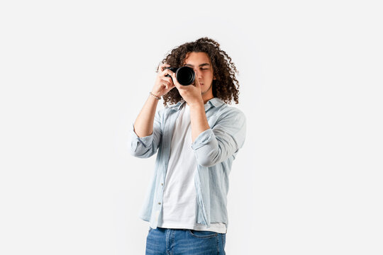 Young man with curly hair is shooting with the camera on his hand. Hobby and photography concept.