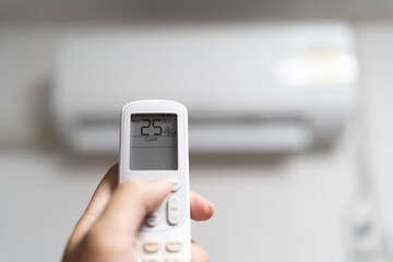 Hand is holding air conditioner remote control, setting temperature 25 Celsius degrees to save energy .