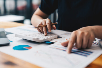 Close up of business woman or accountant hand holding pen working on calculator to calculate business data, accountancy document and laptop computer at office, business concept