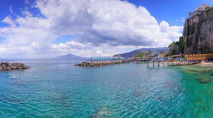 Summertime: Sorrento beach in Italy. View of the jetties lined with beach huts and sun shades by the sea.