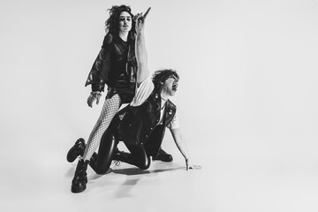 Studio shot of excited, astonished young boy and girl with bright makeup wearing black leather outfits moving on white background. Music, youth