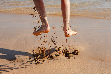 Child with bare feet jumping on the seashore splashing in the wet sand 