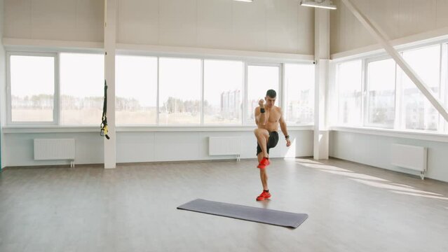Young muscular man warming up in a training in the fitness hall and performing leg raises and jumps
