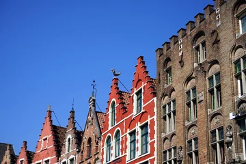 Poster Schöne sanierte bunte alte Fassaden mit Treppengiebel und Burgzinnen vor blauem Himmel im Sonnenschein in den Gassen der Altstadt von Brügge in Westflandern in Belgien © Martin Debus