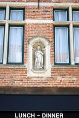 Nische mit Heiligen Statue in der braunen Backstein Fassade eines Restaurant mit Lunch und Dinner...