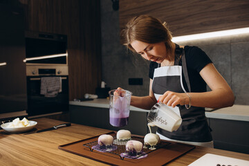 Smiling female confectioner pouring liquid chocolate gommage on biscuit cake. Woman chef in uniform...