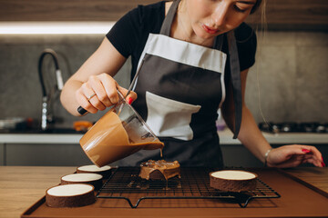 Smiling female confectioner pouring liquid chocolate gommage on biscuit cake. Woman chef in uniform...