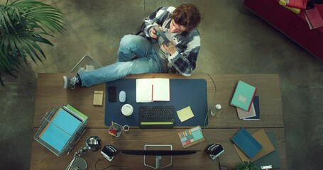 Cinematic top view shot of young male graphic designer or architect is putting on headphones and relaxing by listening his favorite music while working on new project in modern creative studio. - Powered by Adobe