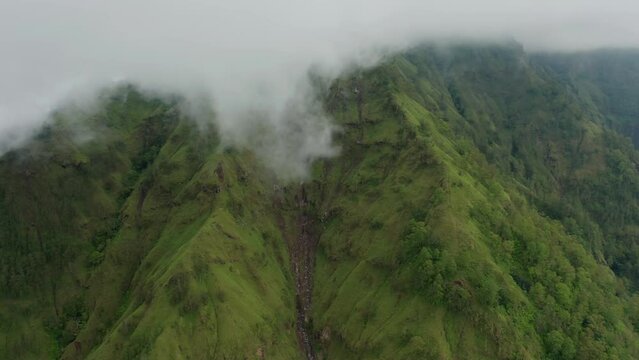 Green caldera mountain walls formed by erosion with clouds above, aerial