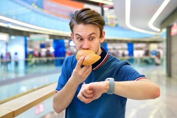 Nervous stressed hungry guy, man in hurry, rush biting, eating big burger, fries and soda look at...