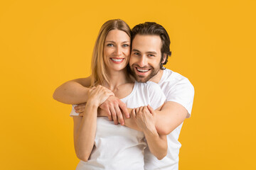 Smiling millennial european husband hugging blond wife in white t-shirt, looks at free space