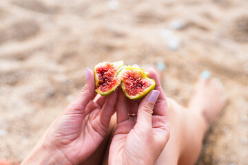 Fototapeta na wymiar A young woman eats a ripe fig on the beach. Vacation and travel concept. Copy cpace. Selective focus.