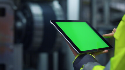 Hands scrolling greenscreen tablet computer on modern production factory.