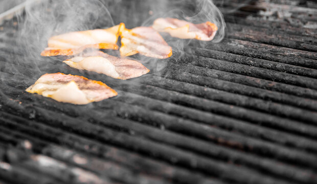 Pork bacon frying on the kitchen grill while smoke
