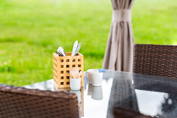 Cutlery and white napkins in a wooden mug on a table in a cozy open coffee on a blurred lawn...