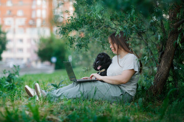Fototapeta premium plus size girl with long brown hair with dog and laptop in park in nature, young woman and pet black poodle