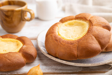 Sour cream bun with cup of coffee on a white wooden background. Side view, selective focus.