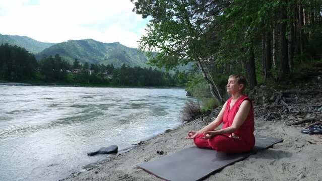 Elderly female meditating in yoga asana near mountain  river flow  