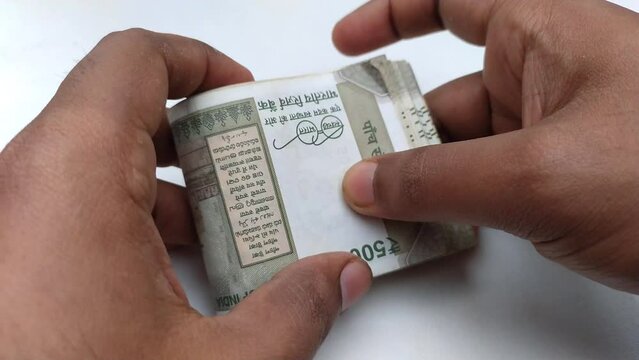 Hand holding stack of indian currency, money or bank notes or bundle of five hundred rupee. Close up 4k macro top view. Financial, savings, business, sucess, profit and investment concept background.