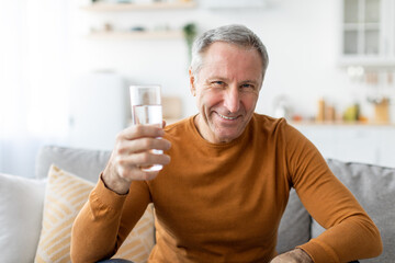 Smiling mature man sitting on couch holding glass of water