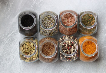 Different types of spices in glass jars. Close up photo of food flavors. Cardamom, turmeric, lavender, curry, pepper and flax seeds. 