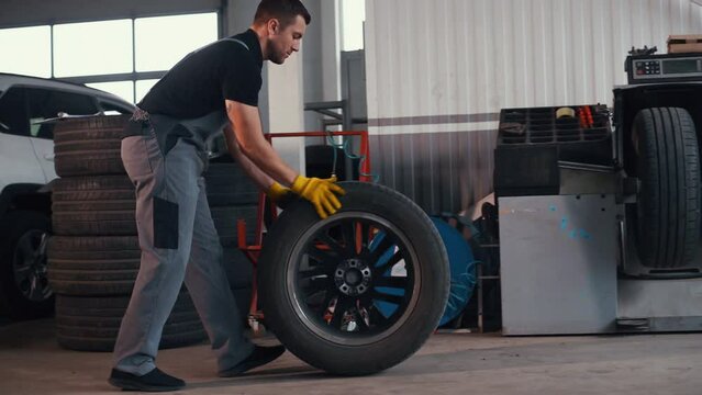 Side view of man in uniform is in the automobile repair shop with new wheel