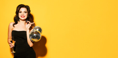 Young brunette woman in evening dress holding champagne and disco ball. Brighrt make up and Wavy...