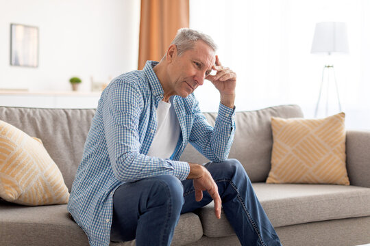 Upset Mature Man Sitting On Couch And Thinking